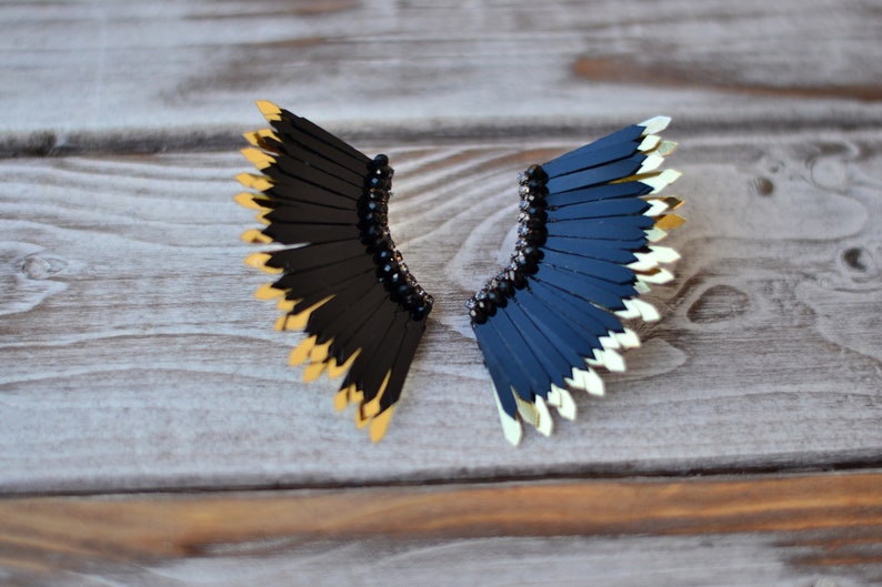 May include: A pair of black and gold earrings with a fan-shaped design. The earrings are made of black feathers with gold tips.