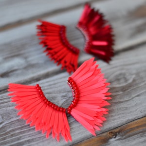 May include: Two pairs of red and pink feather earrings. The earrings are made of layered feathers and have a beaded detail.