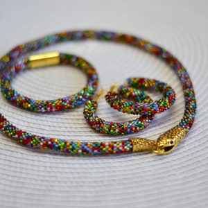 May include: A colourful beaded necklace, bracelet and earrings set with a snake charm. The beads are small and multi-coloured, creating a vibrant and eye-catching look.