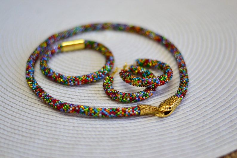 May include: A colourful beaded necklace, bracelet and earrings set with a snake charm. The beads are small and multi-coloured, creating a vibrant and eye-catching look.