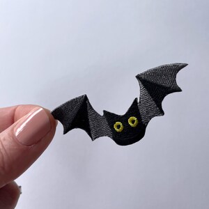 May include: A black felt bat with yellow eyes. The bat is flying with its wings spread out.