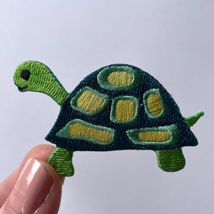 May include: Green and blue embroidered iron-on patch of a cartoon turtle with a shell.