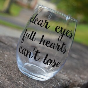Op de afbeelding: Helder glazen wijnglas met de tekst "clear eyes full hearts can't lose" gedrukt op de zijkant.