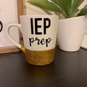Pu&ograve; includere: Una tazza da caff&egrave; bianca con la scritta "IEP prep" in nero e un bordo di glitter dorato.
