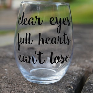 Op de afbeelding: Helder glazen wijnglas met de tekst "clear eyes full hearts can't lose" in het zwart gedrukt.