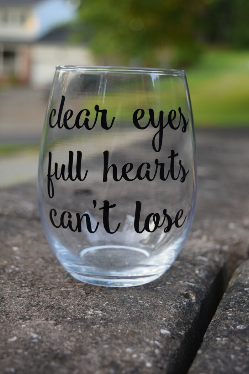Op de afbeelding: Helder glazen wijnglas met de tekst "clear eyes full hearts can't lose" in het zwart gedrukt.