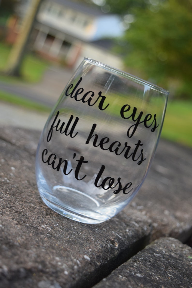 Op de afbeelding: Helder glazen wijnglas met de tekst "clear eyes full hearts can't lose" gedrukt op de zijkant.