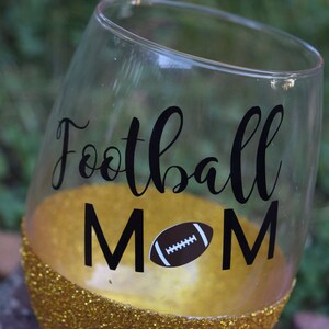 May include: A gold glitter wine glass with a black vinyl decal that says "Football Mom" with a football graphic.