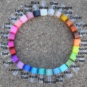 May include: A color chart of glitter in small glass jars. The colors are arranged in a circle, starting with black, white, silver, champagne, gold, copper, pumpkin, espresso, neon orange, neon yellow, neon green, green, mint, light blue, peacock blue, teal, aqua, dark blue, lavender, purple, red, dark pink, petal pink, hot pink, coral, light pink, and light gold.