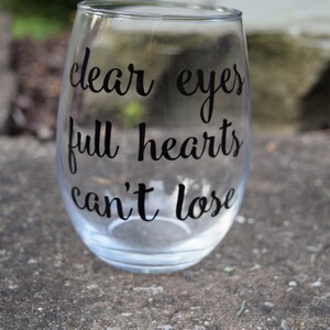 Op de afbeelding: Helder glazen wijnglas met de tekst "clear eyes full hearts can't lose" in het zwart gedrukt.
