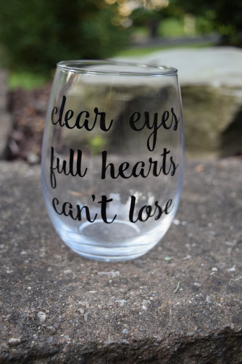 Op de afbeelding: Helder glazen wijnglas met de tekst "clear eyes full hearts can't lose" in het zwart gedrukt.