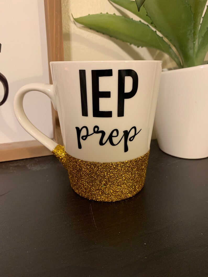 Pu&ograve; includere: Una tazza da caff&egrave; bianca con la scritta "IEP prep" in nero e una fascia di glitter dorati intorno alla base.