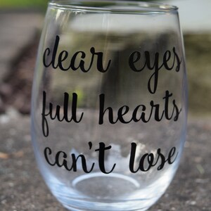 Op de afbeelding: Helder glazen wijnglas met de tekst "clear eyes full hearts can't lose" in het zwart gedrukt.