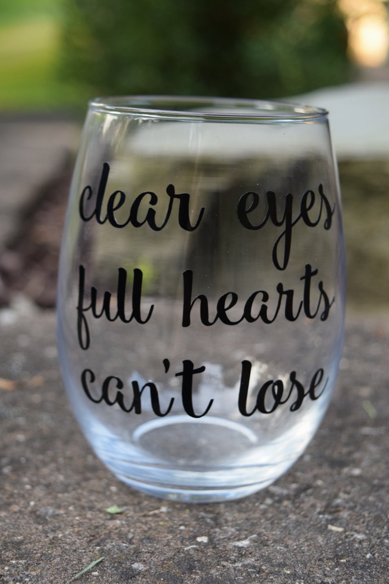 Op de afbeelding: Helder glazen wijnglas met de tekst "clear eyes full hearts can't lose" in het zwart gedrukt.
