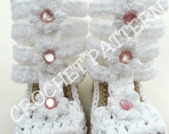 May include: White crocheted baby sandals with pink flower embellishments and a brown sole. The sandals have the text "Hook That Yarn" on the sole.