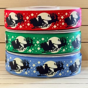 May include: Three spools of grosgrain ribbon stacked vertically, featuring a repeating pattern of a dark silhouette of Santa Claus in a sleigh pulled by reindeer against a white moon, accented with small white stars on red, green, and blue backgrounds.