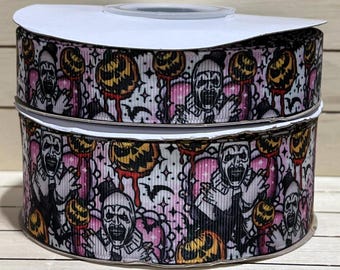 May include: Two spools of white satin ribbon with a pink and black Halloween print. The print features a creepy clown with a jack-o-lantern and bats.