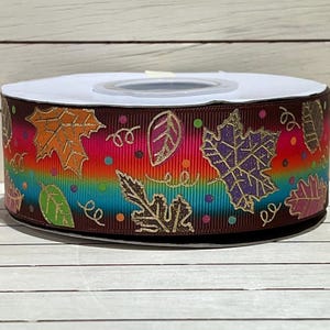 May include: Brown ribbon with a rainbow ombre design and gold foil leaves. The leaves are in various shapes and sizes and are scattered across the ribbon.