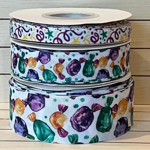 May include: Three spools of white ribbon with different colorful patterns. The top spool has a pattern of confetti, stars, and swirls. The middle spool has a pattern of colorful candy. The bottom spool has a pattern of colorful candy with a white background.