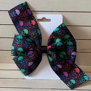 May include: A black hair bow with a colorful skull and star pattern. The bow is attached to a white card.