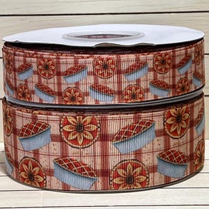 May include: Two spools of decorative ribbon featuring a repeating pattern of pies and sunflowers on a red and cream plaid background. The ribbon is ideal for crafting, gift wrapping, or adding a festive touch to any project.