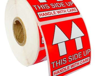Op de afbeelding: Een rol rode en witte verzendetiketten. Elk etiket heeft een witte pijl omhoog, met de tekst "THIS SIDE UP" en "HANDLE WITH CARE" in witte letters.