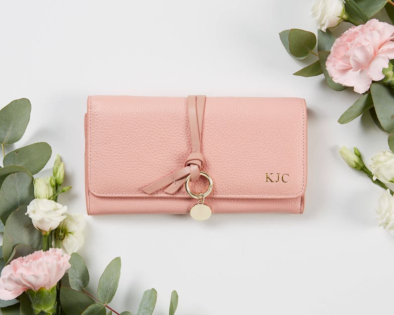 以下が含まれることがあります： ゴールドのチャームと正面に「KJC」のイニシャルが刻印されたピンクの革財布