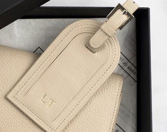May include: A beige leather luggage tag with a gold metal loop and the initials "LT" embossed on the front.
