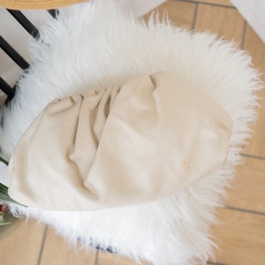 May include: A cream-colored,  soft,  leather clutch bag with a gathered,  pleated design.