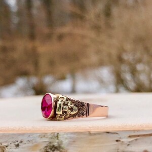 Puede incluir: Un anillo de oro con una gran piedra preciosa ovalada de color rojo oscuro engastada en un engaste ornamentado y detallado.
