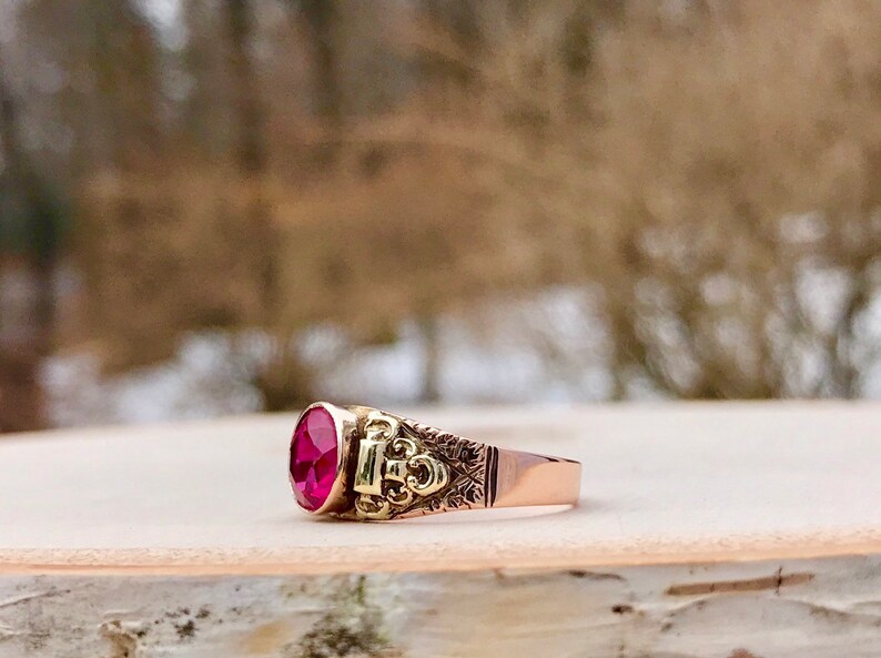 Puede incluir: Un anillo de oro con una gran piedra preciosa ovalada de color rojo oscuro engastada en un engaste ornamentado y detallado.