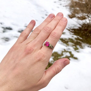 Puede incluir: Un anillo de oro con una piedra ovalada rosa engastada en un dise&ntilde;o de filigrana.