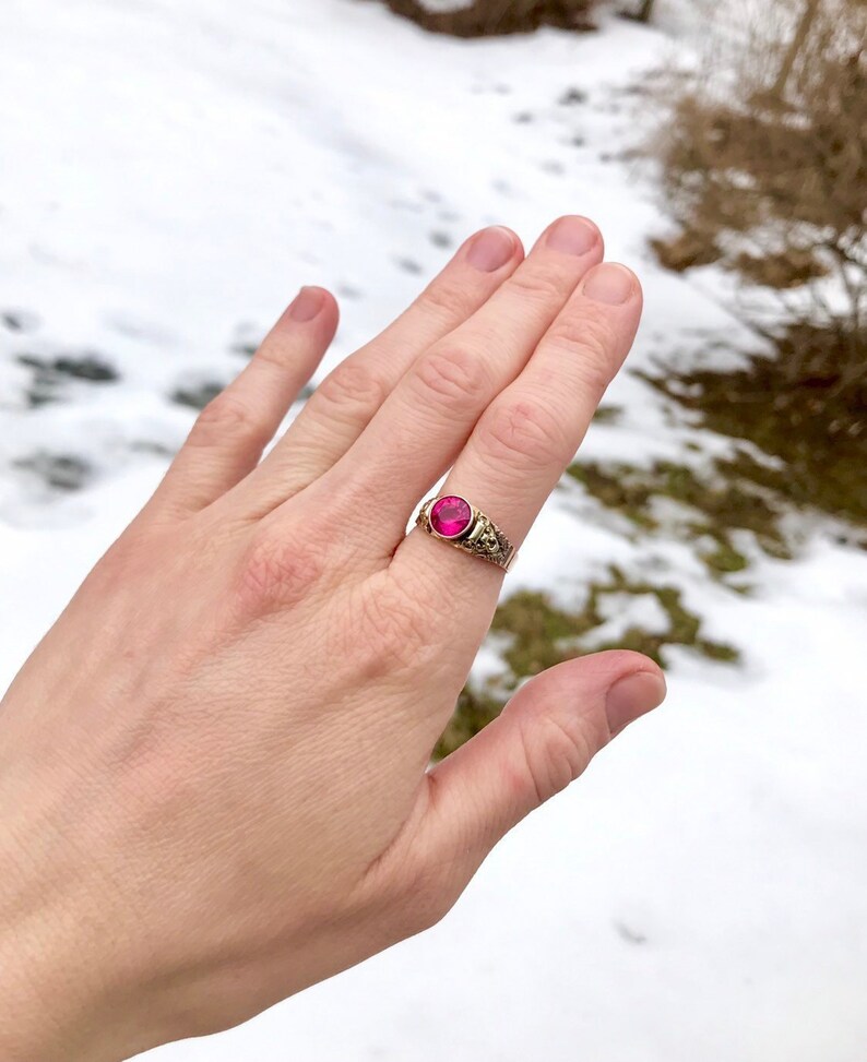 Puede incluir: Un anillo de oro con una piedra ovalada rosa engastada en un dise&ntilde;o de filigrana.