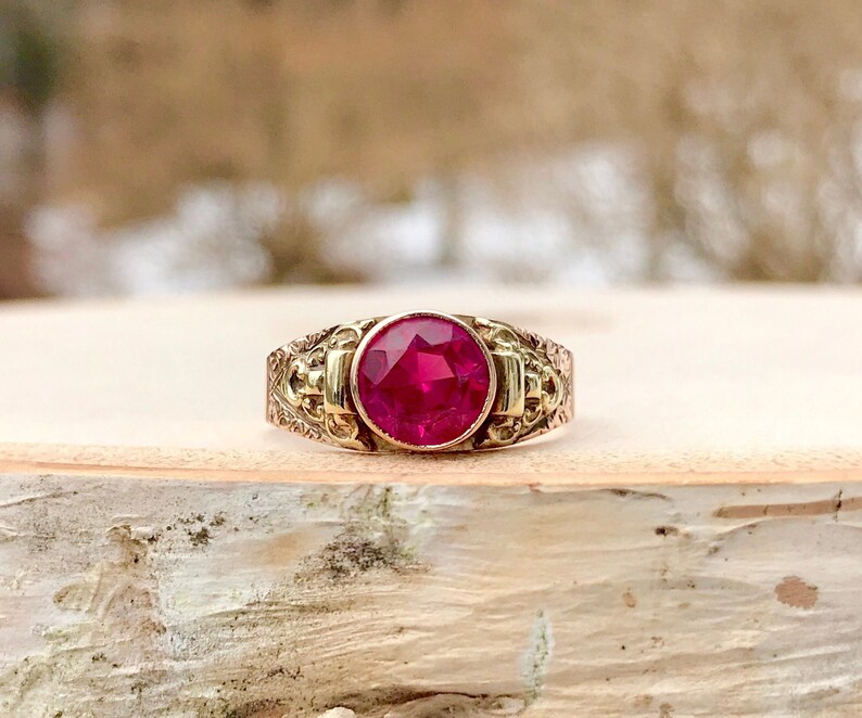 Puede incluir: Un anillo de oro con un dise&ntilde;o adornado y una gran piedra preciosa de rub&iacute; rojo redonda.