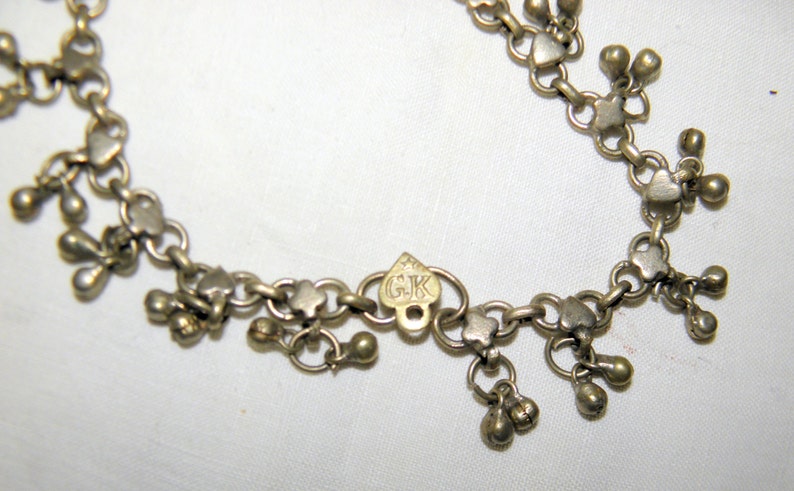 Op de afbeelding: Zilveren ketting met hartvormige schakels en kleine hangende balletjes. De ketting heeft een hartvormig label met de initialen "GK" erop gegraveerd.