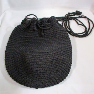 May include: A dark gray crocheted drawstring bag with a round shape and a long, thin strap.