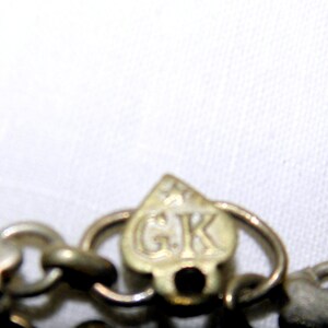 Op de afbeelding: Close-up van een zilveren ketting met een hartvormige sluiting. De sluiting heeft de letters "GK" gegraveerd.