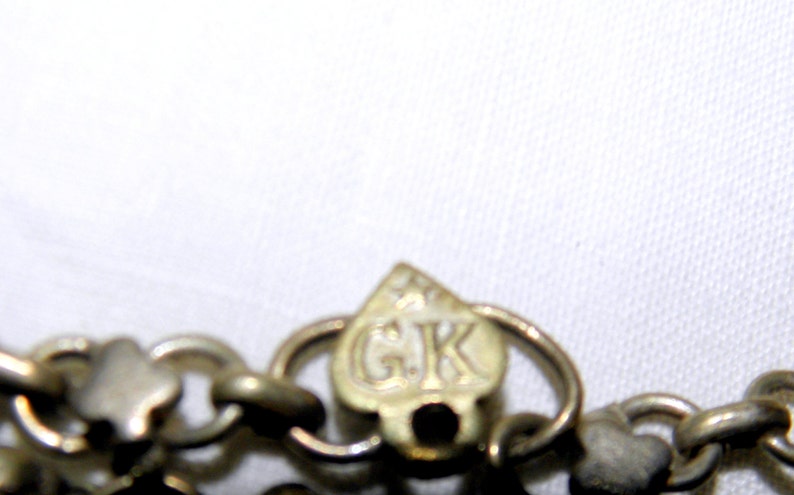 Op de afbeelding: Close-up van een zilveren ketting met een hartvormige sluiting. De sluiting heeft de letters "GK" gegraveerd.