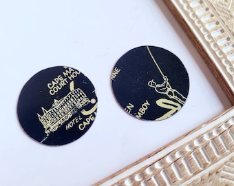 May include: Two round black and gold tokens. One token features a building with the text "Cape May Court House Hotel Cape May". The other token features a stick figure fishing with the text "Ocean City, N.J."