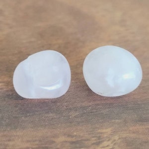 May include: Two white selenite stones, one round and one oval, on a wooden surface.