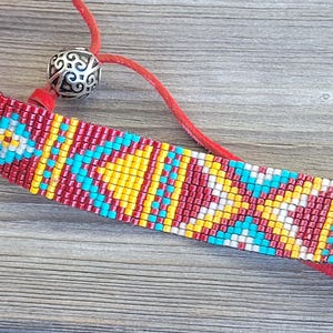 May include: A red, yellow, white, and blue beaded bracelet with a silver bead and a red leather strap.