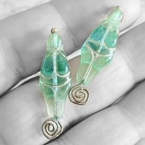 May include: A pair of green glass earrings with a silver spiral dangle. The earrings are shaped like a teardrop and have a textured surface.