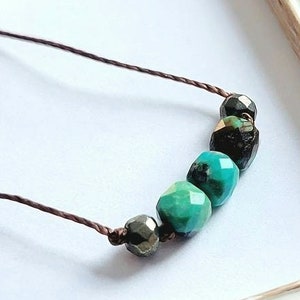 May include: A turquoise and black gemstone necklace with a brown cord. The necklace features five faceted gemstones, including turquoise and black onyx.