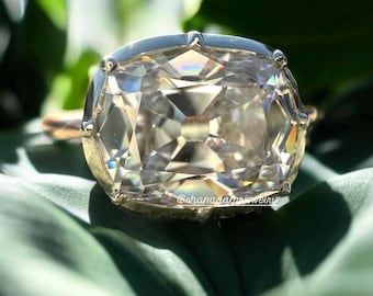 May include: A large, clear, cushion-cut diamond ring set in a silver band. The diamond has a lot of facets and sparkles brightly.