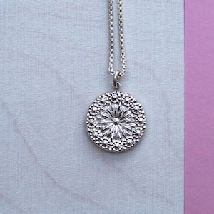 May include: A silver necklace with a round pendant featuring a detailed, starburst design.