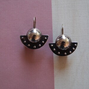 May include: A pair of silver earrings with a round, shiny, silver ball on top of a half-circle base with small silver dots around the edge.