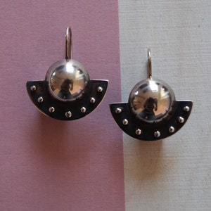 May include: A pair of silver earrings with a half-circle design and a round, reflective ball in the center.