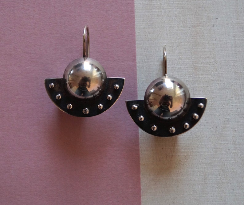 May include: A pair of silver earrings with a half-circle design and a round, reflective ball in the center.
