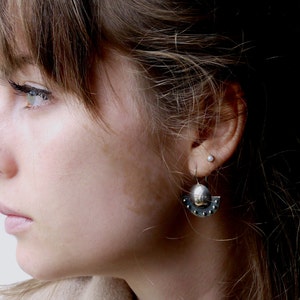 May include: A close-up of a woman's face with a silver earring with a small round charm and a crescent moon design. The earring is in her left ear.