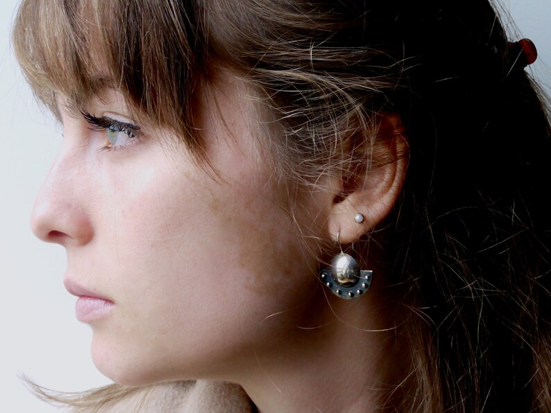 May include: A close-up of a woman's face with a silver earring with a small round charm and a crescent moon design. The earring is in her left ear.